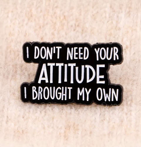 Enamel pin with text 'I don't need your attitude, I brought my own' on a beige background