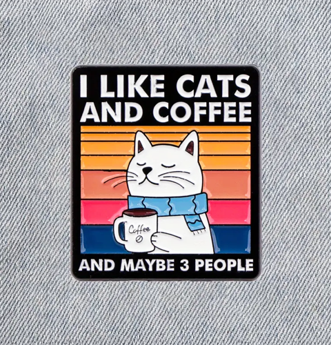 enamel pin with a cat holding a coffee cup and text 'I like cats and coffee and maybe 3 people' on a denim background.