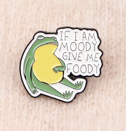 pin with a green character and text 'If I am moody give me foody' on a beige background