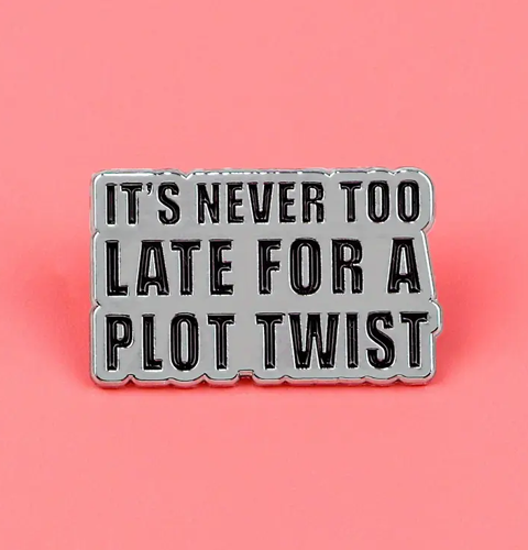 Metallic badge with text 'It's never too late for a plot twist' on a pink background