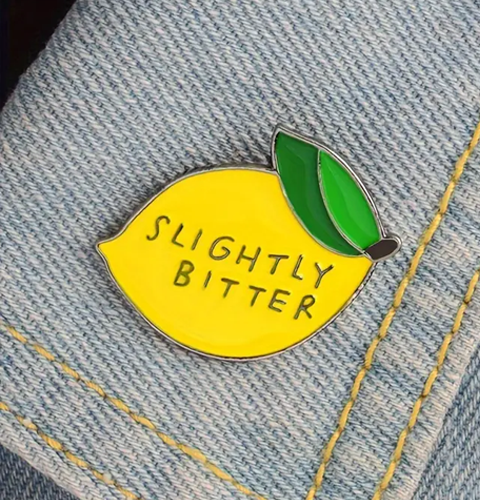Lemon-shaped pin with 'Slightly Bitter' text on a denim background