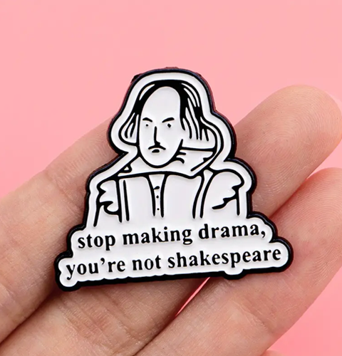 Enamel pin with Shakespeare design and text 'stop making drama, you're not Shakespeare' held in a hand against a pink background.