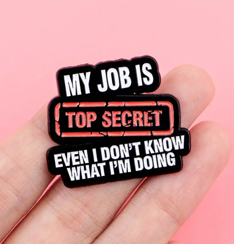 Pin with 'My job is top secret even I don't know what I'm doing' text held in a hand against a pink background